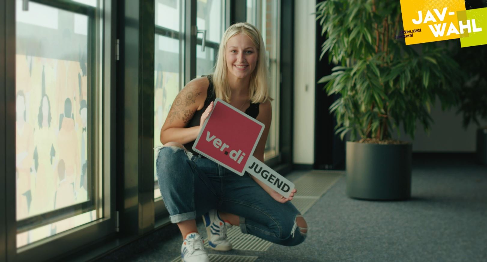 junge Frau in Hocke mit ver.di Jugend Schild in der Hand