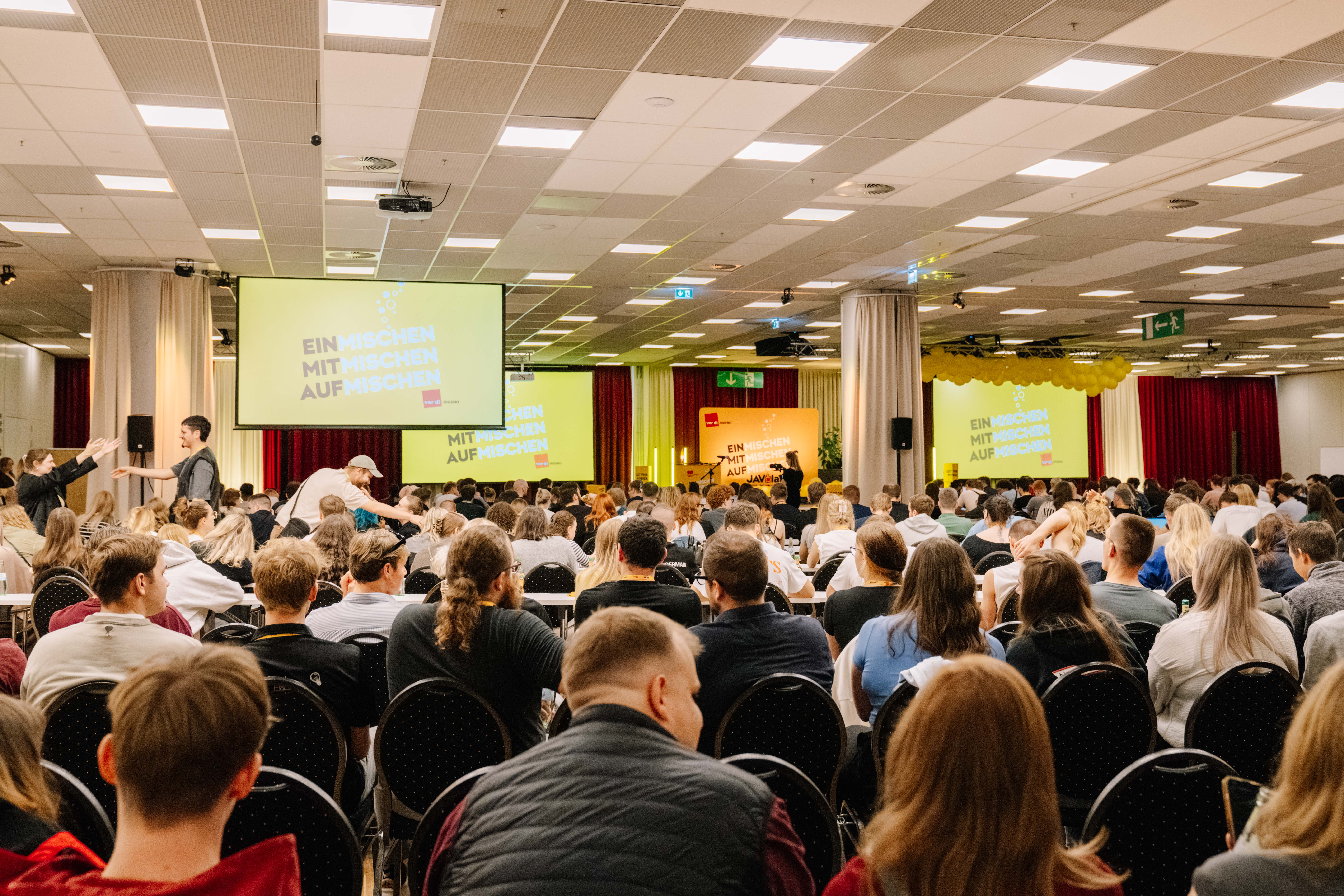 Viele Personen sitzen auf einer Konferenz und schauen zur Bühne.