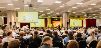 Viele Personen sitzen auf einer Konferenz und schauen zur Bühne.